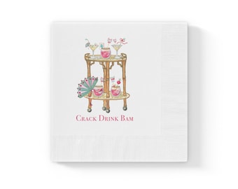 May include: A white paper napkin featuring a watercolour illustration of a two-tiered bamboo bar cart holding pink cocktails, a decorative fan, and stirrers. The text CRACK DRINK BAM is printed in pink below the bar cart illustration.