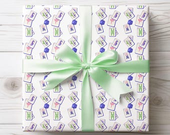 May include: A square gift box wrapped in white paper featuring a repeating pattern of colorful mahjong tiles and small blue dice. The box is tied with a wide, smooth, light green satin ribbon arranged in a decorative bow across the center.