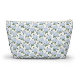 Puede incluir: Una bolsa blanca con cremallera con un patrón repetido de flores de hortensias azules sobre un fondo blanco.