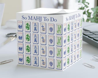May include: A white cube-shaped notepad with a Mahjong theme. The notepad features various Mahjong tile designs in green, blue, and white, with the text "So MAHJ To Do" printed on the top. The notepad is on a white surface.