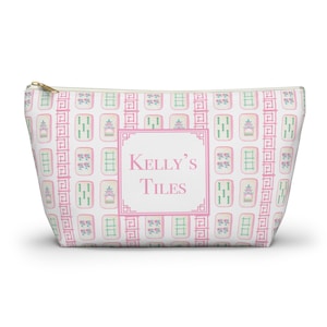 Puede incluir: Una bolsa blanca con cremallera con un patrón rosa y verde de fichas de mahjong. La bolsa tiene el texto "Kelly's Tiles" en rosa.