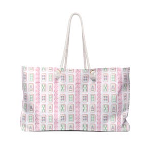 May include: A large white tote bag with a repeating pattern of pink, green, and white Mahjong tiles. The bag has a white rope handle and is designed for carrying items. The bag is rectangular and has a large capacity.