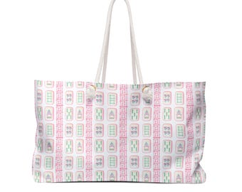 May include: A large white tote bag with a repeating pattern of pink, green, and white Mahjong tiles. The bag has a white rope handle and is designed for carrying items. The bag is rectangular and has a large capacity.