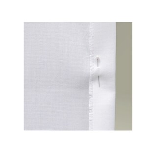May include: A piece of solid white fabric with a visible woven texture. The right edge of the fabric is folded over, creating a hemmed appearance with a frayed, raw edge visible along the fold. Two straight sewing pins are inserted vertically.