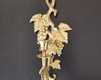 May include: Gold-toned metal wall sconce with a grapevine design. The sconce has a single candle holder and is perfect for adding a touch of elegance to any room.