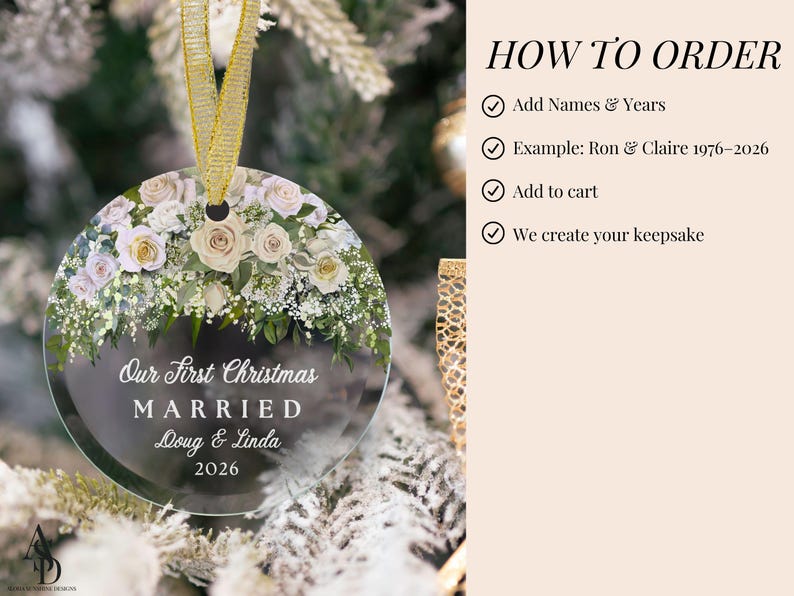 K&ouml;nnte beinhalten: Ein runder, durchsichtiger Acryl-Weihnachtsbaumschmuck mit einem Blumenarrangement aus wei&szlig;en und blassrosa Rosen sowie gr&uuml;nem Blattwerk. Der Text lautet: Our First Christmas MARRIED Doug & Linda 2026. Ein goldenes Band ist oben zum Aufh&auml;ngen befestigt.