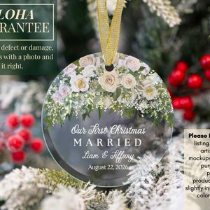 K&ouml;nnte beinhalten: Ein runder, klarer Glasanh&auml;nger mit einem Blumenarrangement aus wei&szlig;en und blassrosa Rosen sowie gr&uuml;nem Blattwerk am oberen Rand. Der Text lautet: Our First Christmas MARRIED, Liam & Tiffany, August 22, 2026. Er h&auml;ngt an einem goldenen Band.