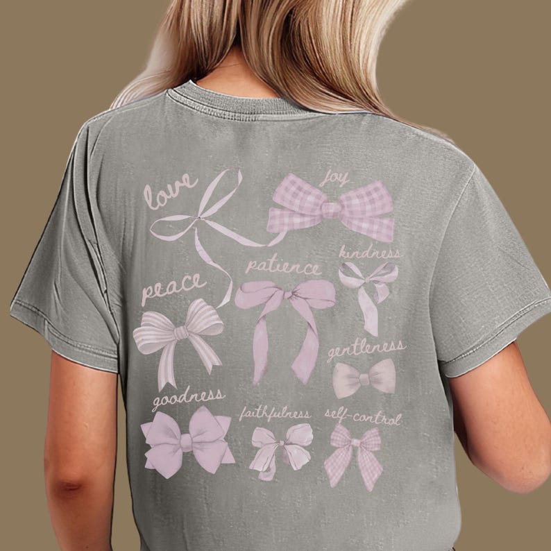 May include: Grey t-shirt with a design of pink bows and words such as "love", "peace", and "joy". The shirt has a vintage, faded appearance.