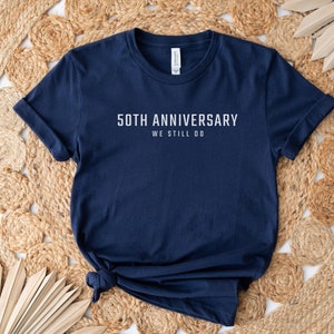 May include: A navy blue t-shirt with white text that reads "50th Anniversary We Still Do".