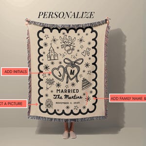 May include: A beige personalized wedding blanket with a black scalloped border. The blanket features a heart design with initials, wedding-themed illustrations, and the text "Married The Martins November 11, 2025".