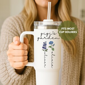 May include: White travel mug with a black lid and a straw. The mug has a floral design with the text "gigi's garden" and the names "oliver" and "olivia" written vertically.