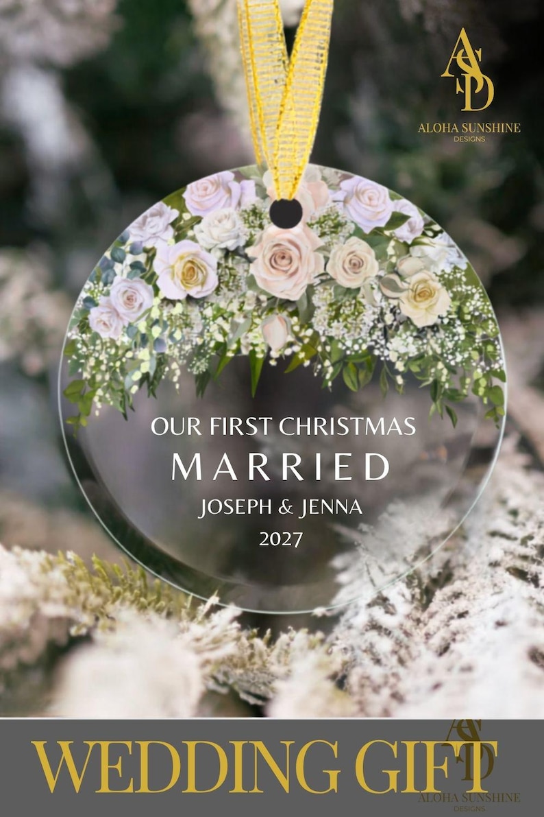 K&ouml;nnte beinhalten: Ein rundes, transparentes Acryl-Ornament mit einem Blumenarrangement aus blassrosa und wei&szlig;en Rosen sowie gr&uuml;nem Blattwerk am oberen Rand. Der Text lautet OUR FIRST CHRISTMAS MARRIED JOSEPH & JENNA 2027. Ein goldenes Band ist oben befestigt.