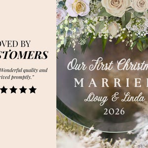 K&ouml;nnte beinhalten: Ein kreisf&ouml;rmiges Ornament aus klarem Acryl mit einem Blumenarrangement aus wei&szlig;en und blassrosa Rosen mit gr&uuml;nen Bl&auml;ttern an der Oberseite. Der Text lautet Our First Christmas MARRIED Doug & Linda 2026. Links steht der Text LOVED BY CUSTOMERS.