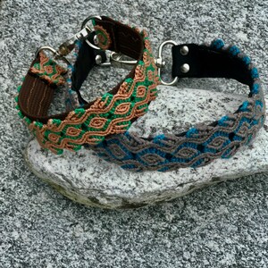 May include: Two dog collars with a woven pattern. The top collar is brown with green and tan woven into the pattern. The bottom collar is gray with blue and tan woven into the pattern.