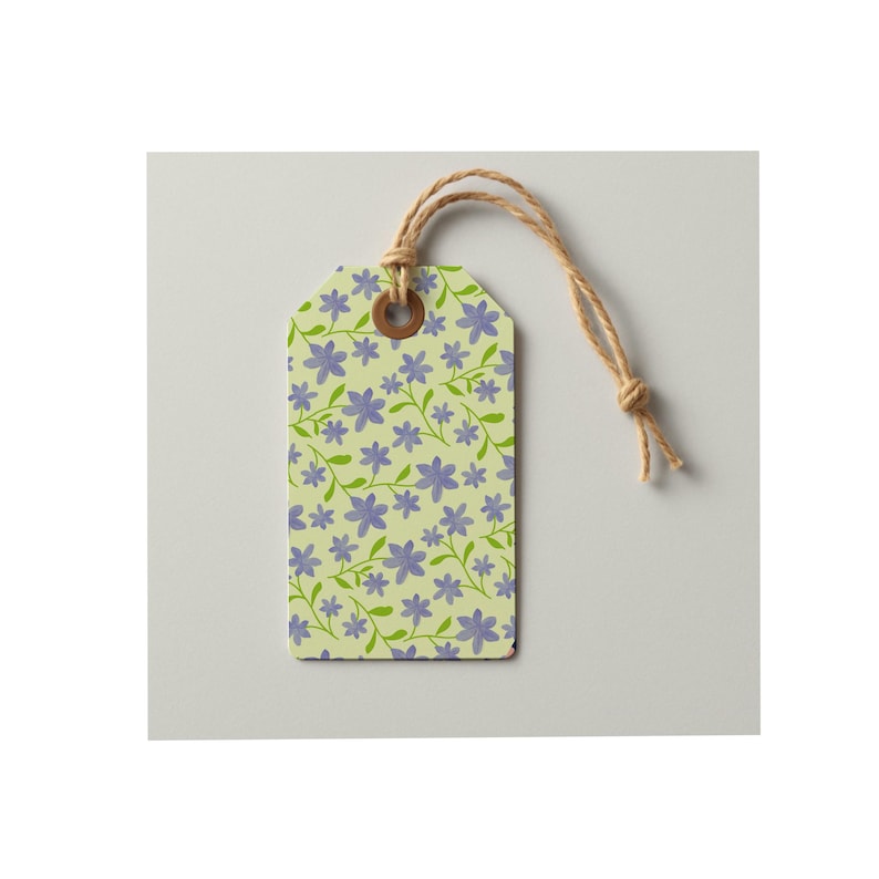 May include: A rectangular paper gift tag featuring a light yellow background with a repeating pattern of small purple flowers and green stems. The tag has a brown reinforced eyelet at the top with a piece of natural tan twine looped through it.