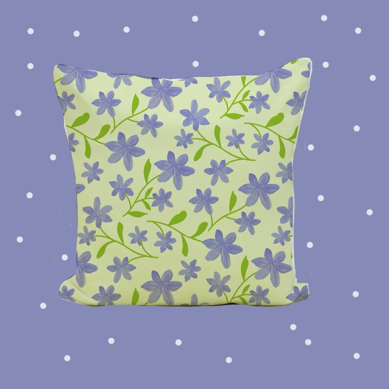 May include: A square throw cushion featuring a light lime green background with a repeating pattern of purple six-petalled flowers and thin green stems with small leaves. The design covers the entire front surface of the cushion in a consistent layout.