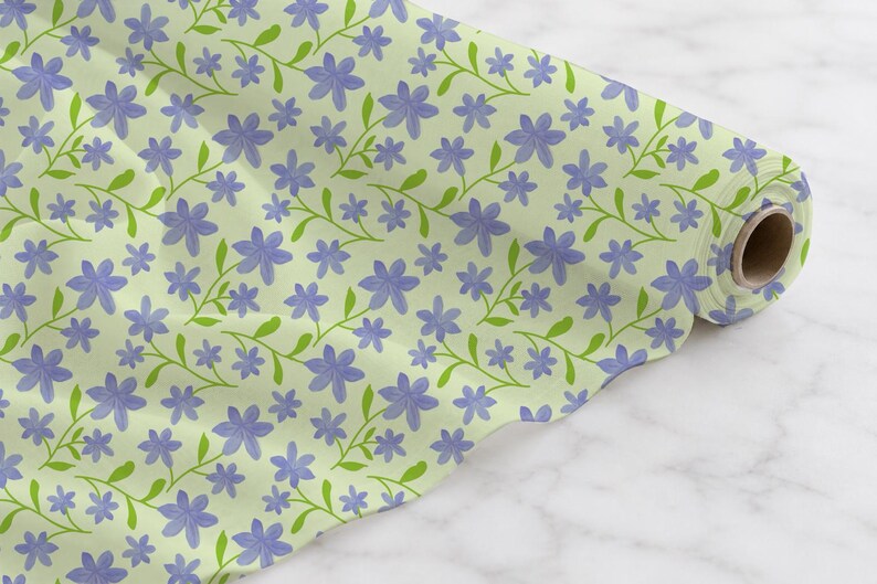 May include: A roll of fabric featuring a repeating pattern of light purple five-petalled flowers with green stems and leaves on a pale lime green background. The fabric is wound around a central cardboard tube, displaying a continuous floral print.