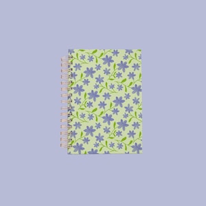 May include: A spiral-bound notebook featuring a light green cover with a repeating pattern of small purple flowers and thin green stems. The binding consists of a metallic copper-coloured wire coil along the left side of the rectangular notebook.