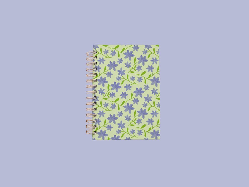 May include: A spiral-bound notebook featuring a light green cover with a repeating pattern of small purple flowers and thin green stems. The binding consists of a metallic copper-coloured wire coil along the left side of the rectangular notebook.