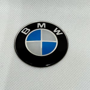Op de afbeelding: Een cirkelvormig BMW-embleem. Het logo heeft een zwarte rand met de letters "B", "M" en "W" in het wit. Het midden heeft een zilver en blauw segmentontwerp.