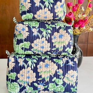 May include: A stack of three rectangular quilted pouches in varying sizes, featuring a dark navy blue fabric with a repeating pattern of light peach flowers and green leaves. Each pouch has a zipper closure with small striped fabric tabs at the ends.