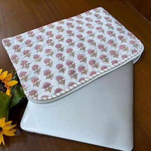 Peut inclure: Une housse pour ordinateur portable blanche avec une fermeture éclair. La housse est décorée d'un imprimé floral rose et blanc.