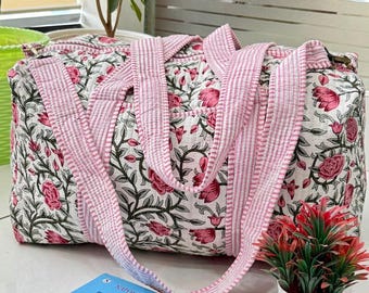 May include: A floral print tote bag with pink and white striped handles. The bag features a white background with a pattern of pink flowers and green leaves. A book titled "Think & Grow Rich" is visible.