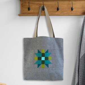 May include: A gray canvas tote bag with a green, blue, and turquoise star-shaped design. The bag has two long straps.