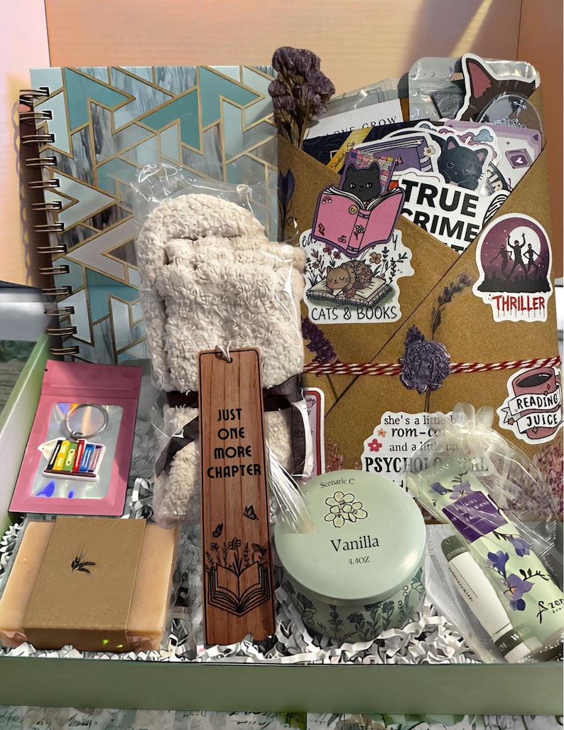Pu&ograve; includere: Una confezione regalo contenente un taccuino a spirale con motivo geometrico blu, un paio di calzini beige felpati, un segnalibro in legno con la scritta "JUST ONE MORE CHAPTER", una candela alla vaniglia in barattolo da 125g, sapone, portachiavi e adesivi.