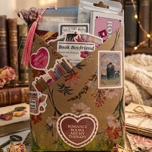 Pu&ograve; includere: Una busta di carta marrone decorata con motivi floreali e vari adesivi, tra cui un'etichetta a forma di cuore con la scritta ROMANCE BOOKS ARE MY THERAPY, un adesivo con Book Boyfriend e un adesivo rosa con ENEMIES TO LOVERS.