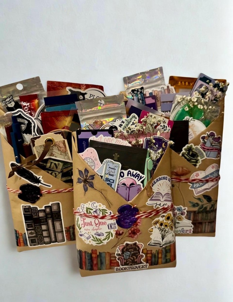 Pu&ograve; includere: Tre buste di carta marrone riempite con vari articoli a tema librario, tra cui adesivi, segnalibri e piccoli pacchetti. Ogni busta &egrave; legata con uno spago rosso e bianco e sigillata con ceralacca, decorata con illustrazioni di libri.