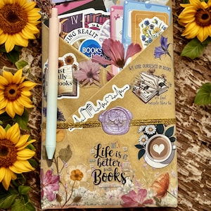 Pu&ograve; includere: Una busta di carta marrone riempita con adesivi, cartoline e una spilla con la scritta No shelf control. Una penna color pastello &egrave; fissata sul lato. La busta presenta illustrazioni floreali, un sigillo in ceralacca e il testo Life is better with Books.