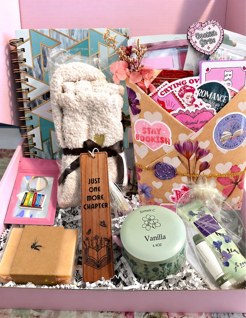 Pu&ograve; includere: Una confezione regalo contenente un taccuino a spirale con motivo geometrico verde acqua, un paio di calzini beige soffici, un segnalibro in legno con la scritta "JUST ONE MORE CHAPTER", una candela alla vaniglia, una saponetta, un portachiavi e una busta decorata.