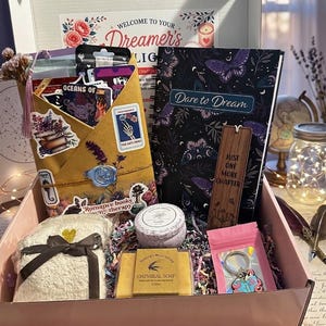 Pu&ograve; includere: Una scatola regalo contenente un libro intitolato Dare to Dream, un segnalibro in legno con il testo Just One More Chapter, una busta color marrone chiaro con adesivi e un sigillo in cera blu, una candela alla vaniglia, un sapone all'avena e un portachiavi.