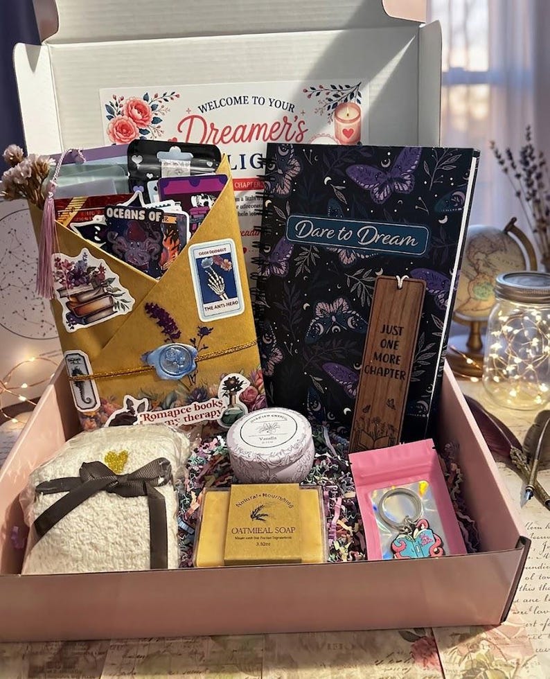 Pu&ograve; includere: Una scatola regalo contenente un libro intitolato Dare to Dream, un segnalibro in legno con il testo Just One More Chapter, una busta color marrone chiaro con adesivi e un sigillo in cera blu, una candela alla vaniglia, un sapone all'avena e un portachiavi.