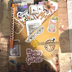 Pu&ograve; includere: Una busta di carta marrone riempita con vari adesivi tra cui un teschio, un libro aperto, occhiali, un orologio e una boccetta. La busta &egrave; legata con dello spago, presenta un sigillo di ceralacca dorato e il testo Mystery Thriller Girlie.