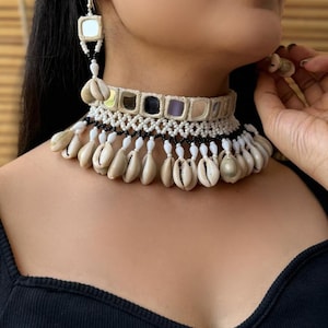 May include: A handcrafted necklace and earring set featuring a choker-style necklace with mirror accents, black and white beading, and dangling seashells. The matching earrings have a similar design. The jewelry is a bohemian style.