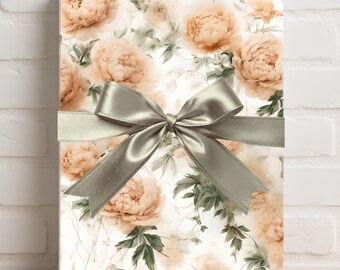 Peut inclure: Un coffret cadeau enveloppé dans du papier à motifs floraux de pivoines pêche et de feuilles vertes sur fond blanc. Un ruban de satin argenté est noué en nœud autour du coffret, pour une présentation élégante.