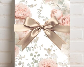 Peut inclure: Un coffret cadeau rectangulaire enveloppé de papier floral avec des pivoines roses et du feuillage vert. Un ruban et un nœud en satin couleur champagne sont attachés autour de la boîte, créant une présentation décorative. Le coffret est posé contre un mur de briques blanches.