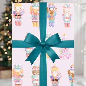 Puede incluir: Un regalo envuelto con un lazo verde azulado. El papel de regalo es rosa claro y presenta un patrón repetido de soldados cascanueces de acuarela en varios colores. Un árbol de Navidad es visible en el fondo.
