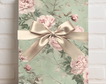 Puede incluir: Una caja de regalo envuelta en papel floral con peonías rosas y hojas verdes. Una cinta de raso dorada está atada con un lazo alrededor de la caja. El fondo es de color verde claro.