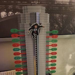 May include: A 3D printed model of the Nakatomi Plaza building from the movie Die Hard. The building is gray and has red and green numbers on the side. The model is on a black base with the words "Die Hard" printed in red.