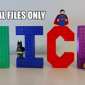 Könnte beinhalten: Ein Satz aus vier bunten, 3D-gedruckten Buchstaben, die "NICK" buchstabieren, mit Lego-Minifiguren von Superman, Batman und Robin, die vor den Buchstaben stehen. Die Buchstaben sind so gestaltet, dass sie wie Lego-Steine aussehen.