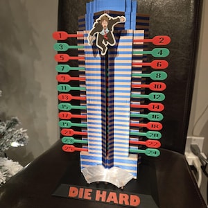 May include: A 3D-printed advent calendar shaped like a skyscraper, with red and green numbered pegs. The words "DIE HARD" are printed on the base. A figure of a man is attached to the building.