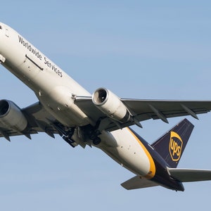 May include: A white Boeing 757-200 cargo plane with the words "Worldwide Services" on the side and the UPS logo on the tail. The plane is in flight and the landing gear is down.