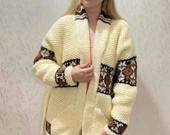 May include: A cream-colored knitted cardigan with brown and white geometric patterns. The cardigan has a shawl collar, long sleeves, and a tie belt.