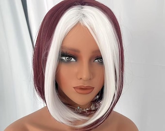 May include: A short, straight bob wig with burgundy and white streaks. The wig is styled with a side parting and the ends are slightly flipped out. The wig is on a mannequin head. The text "BAG Wigs" is on a white tag in front of the wig.