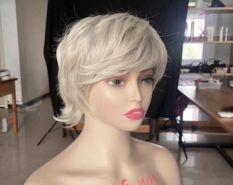 May include: A short, platinum blonde wig with a side parting and choppy layers. The wig is styled on a mannequin head with the text "BAG wig" written on the chest.