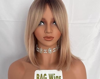 May include: A blonde wig with a side parting and blunt cut bangs. The wig is styled in a straight, shoulder-length bob. The wig is on a mannequin head with a white background. The text "BAG Wigs" is on a label in front of the mannequin.