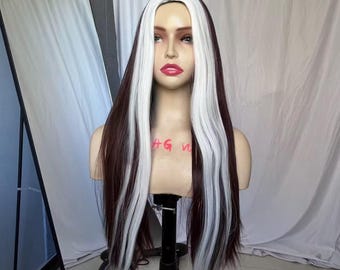 May include: A long, straight synthetic wig featuring dark brown hair with prominent, thick white streaks framing the face. The wig is displayed on a mannequin head, showcasing a center part and smooth, layered strands that fall past the shoulders.
